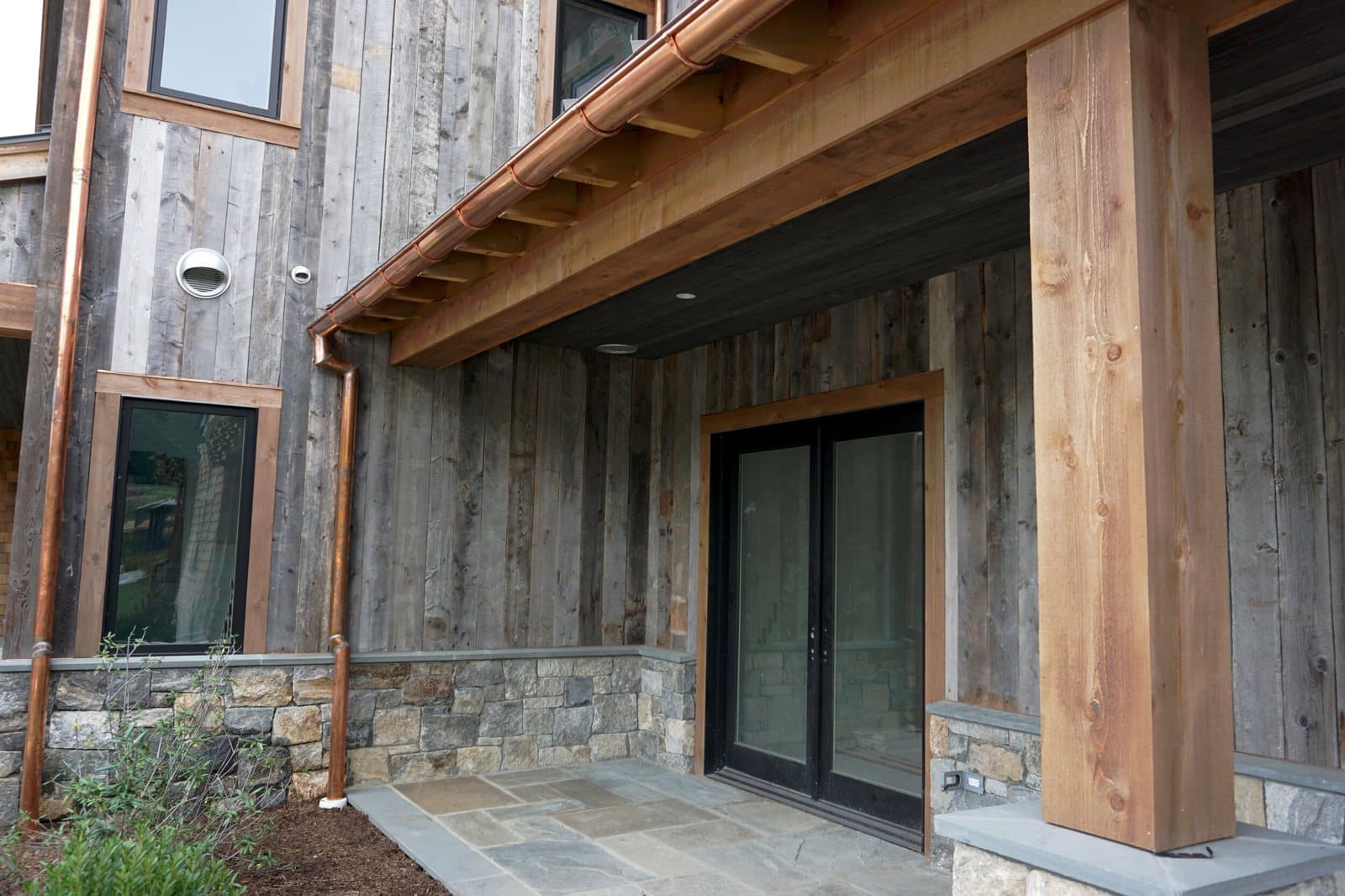 Reclaimed corral and gray board cladding on a premium home exterior with stone base